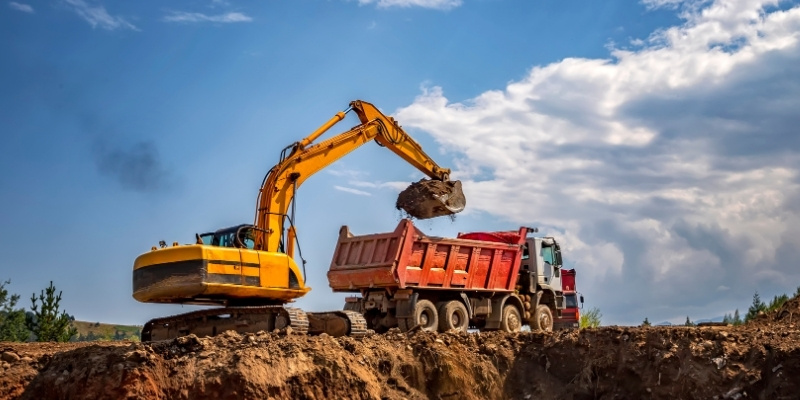 backhoe putting soil in a roll off container